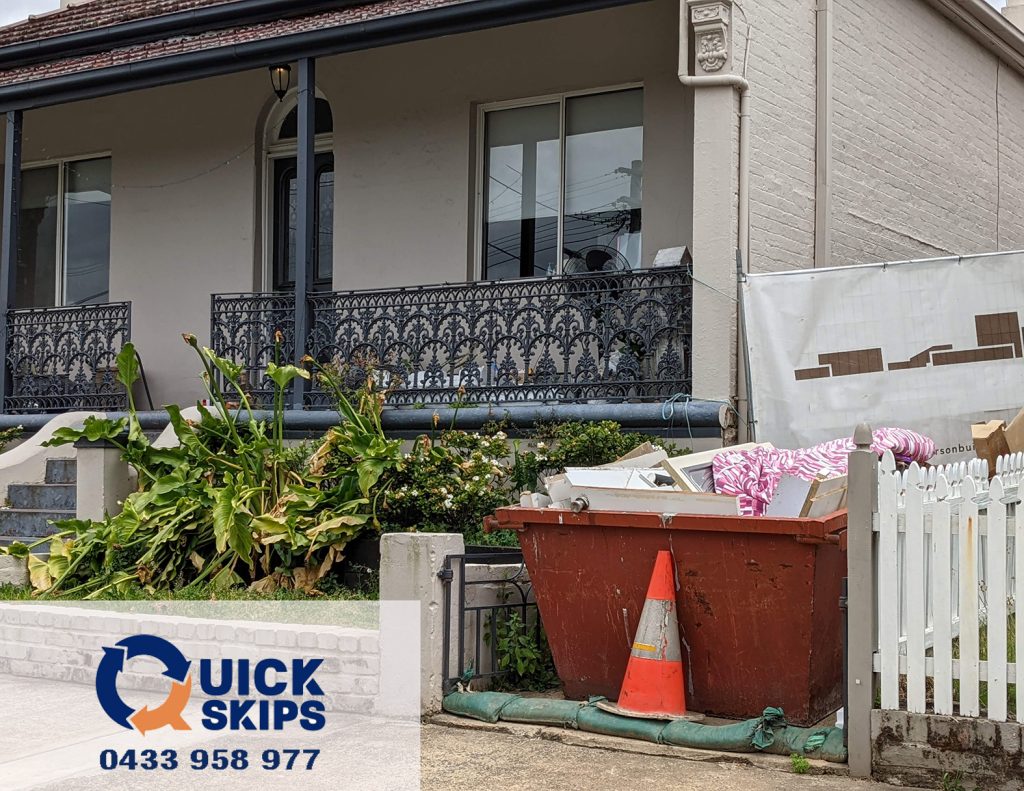 small 2 cubic meter skip bin with no door on rear side placed in driveway, while the builder is clearing out the debris from the house